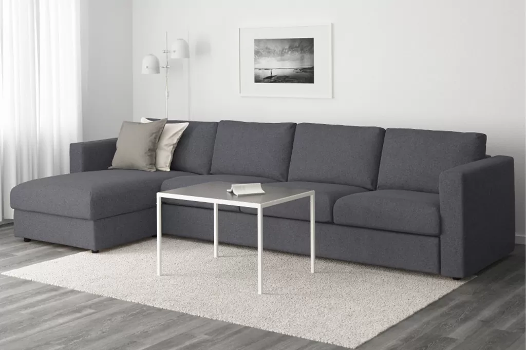Просторий сірий кутовий диван у мінімалістичному інтер’єрі з білими стінами, світлою підлогою та сучасним декором