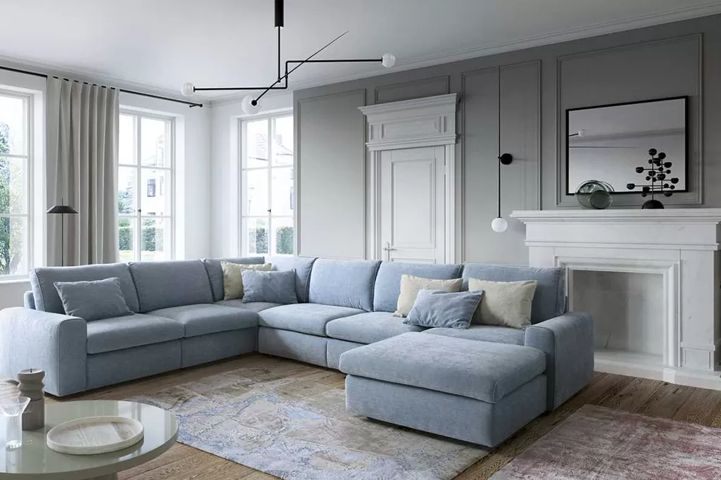 Світла простора вітальня в класичному стилі з великим блакитним диваном, декоративними подушками та каміном із білого мармуру.