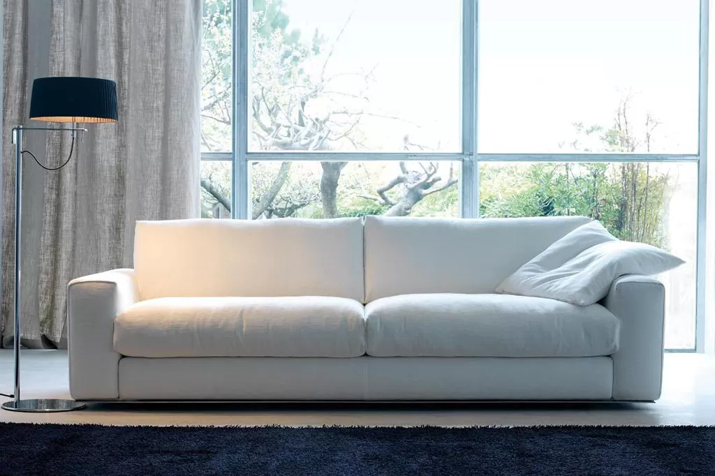 Мінімалістичний білий диван із пухкими подушками у світлій кімнаті з панорамними вікнами та торшером