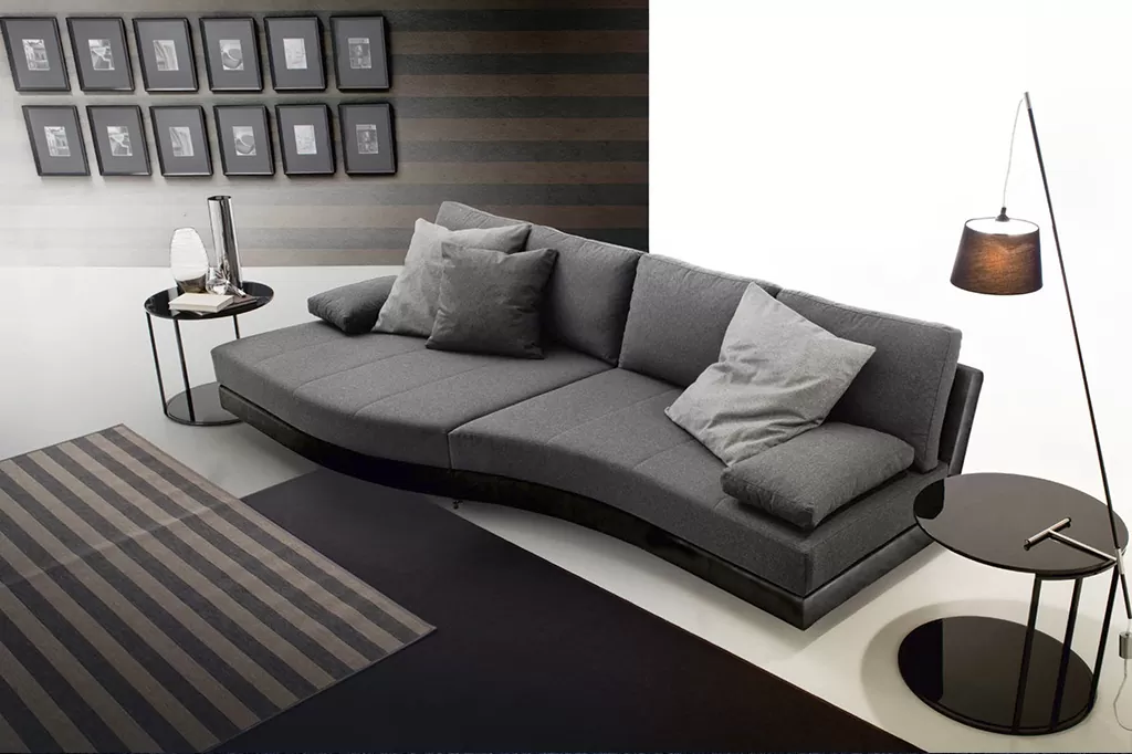 Стильний вигнутий диван у темно-сірому кольорі з подушками, розташований у сучасному мінімалістичному інтер’єрі