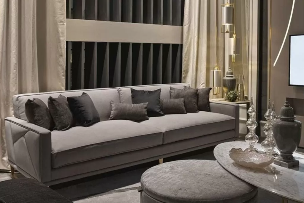 Стильна вітальня з неокласичним сірим диваном, контрастними подушками, мармуровим столиком і декоративними світильниками.