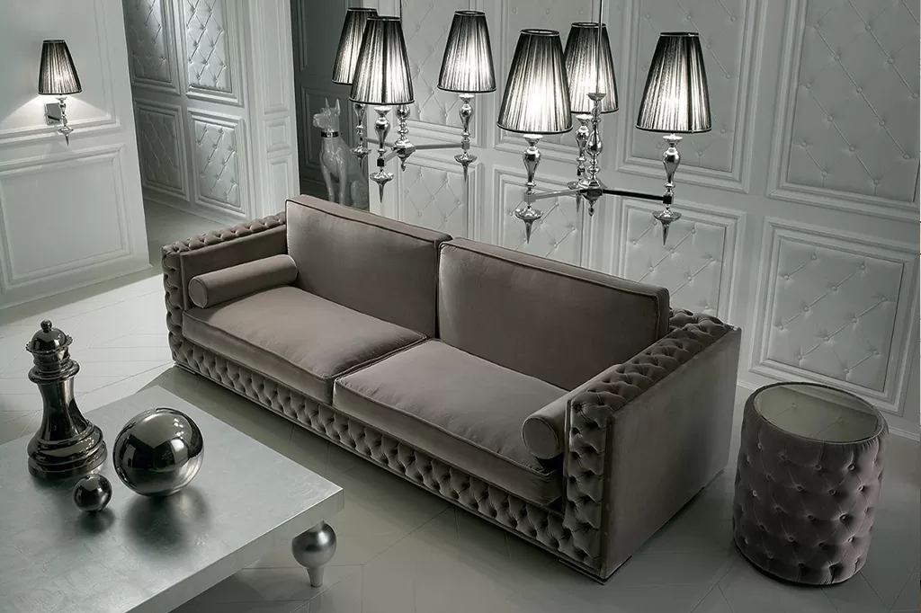 Елегантний класичний диван із велюровою оббивкою та каретною стяжкою в інтер’єрі зі сріблястими лампами та декоративними панелями.